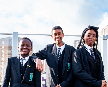 Three smiling students standing in an outdoor area